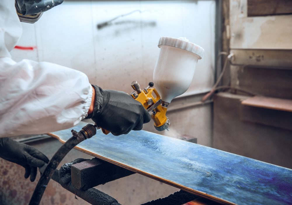 Master painter in a factory - industrial painting wood with spray gun.